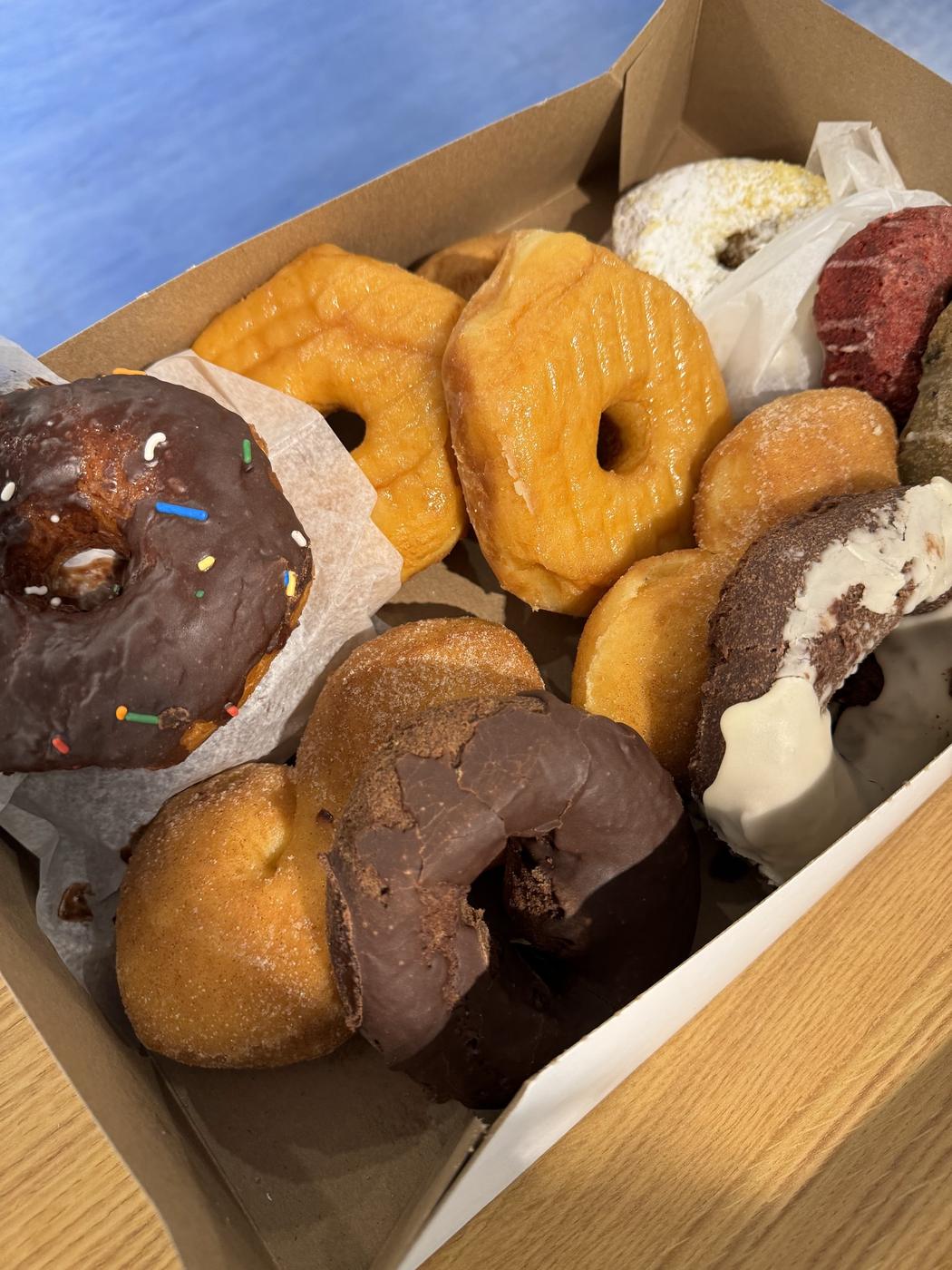 A box of donuts from World's Fair Donuts including a sprinkled ring, chocolate iced rings and plain cake rings