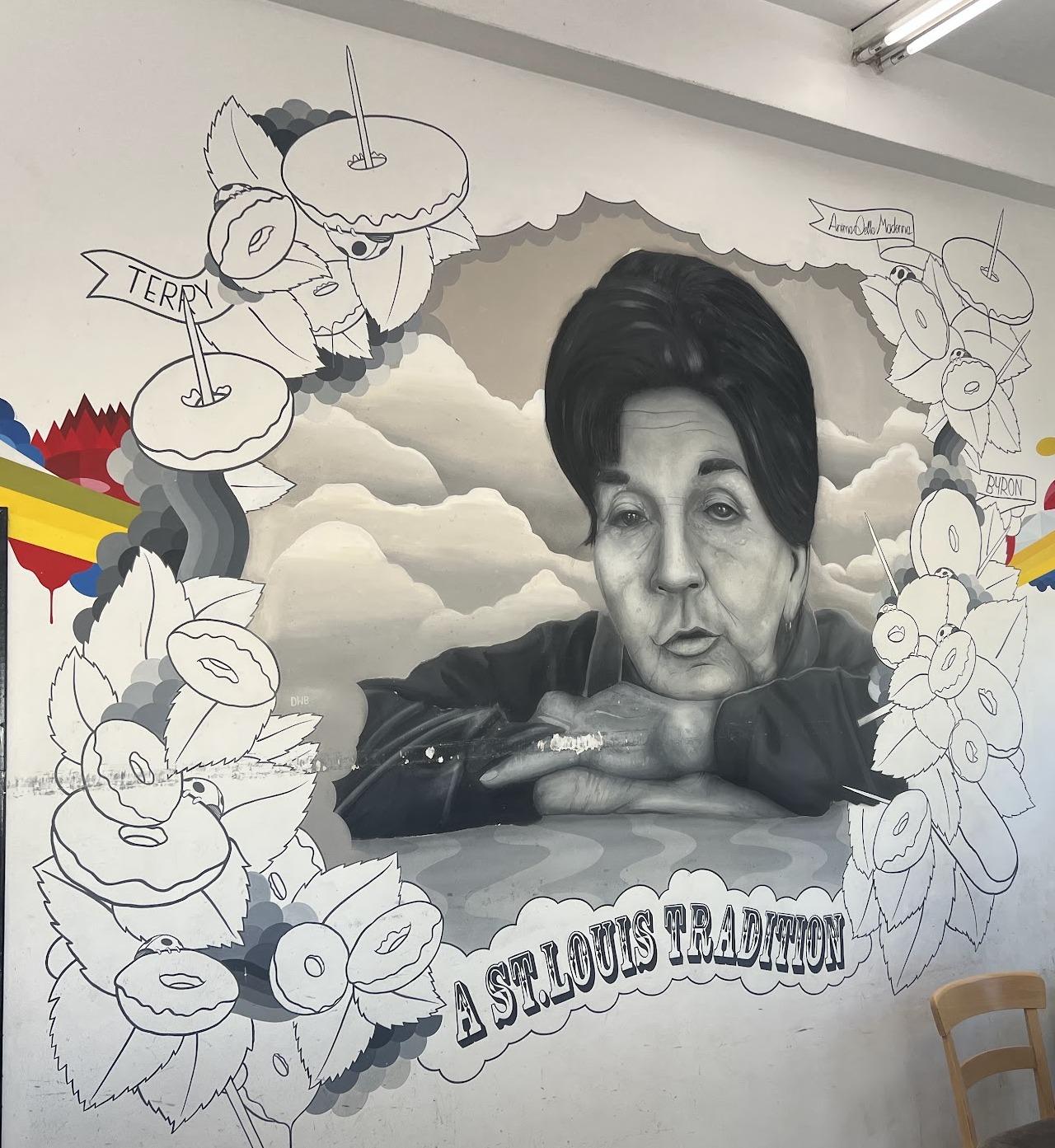 The mural inside World's Fair Donuts: a painted portrait among clouds surrounded by drawn donuts, with a banner reading A ST. LOUIS TRADITION