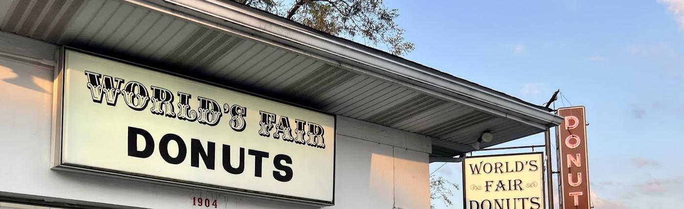 The World's Fair Donuts storefront sign: WORLD'S FAIR in an ornate serif over DONUTS in heavy black letters, with the street number 1904 painted beneath
